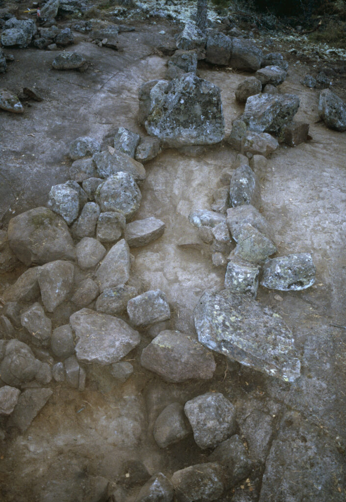 Kuvassa näkyy kaksi kivistä rakennettua suorakaiteen muotoista rakennelmaa, joissa on on päädyissä isommat pystykivet, sekä keskellä yksi yhteinen päätykivi.