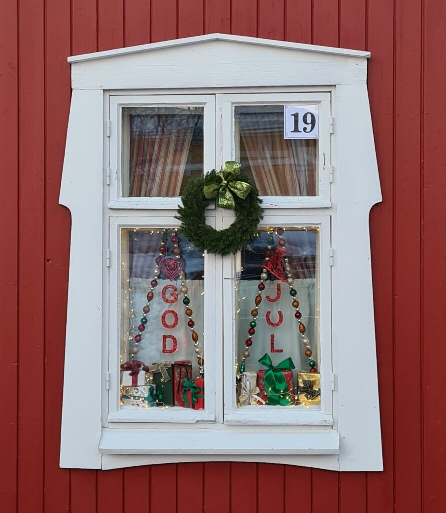 Joulukalenteri-ikkuna nro. 19 punaisessa talossa valkokarminen ikkuna jossa somistuksia.