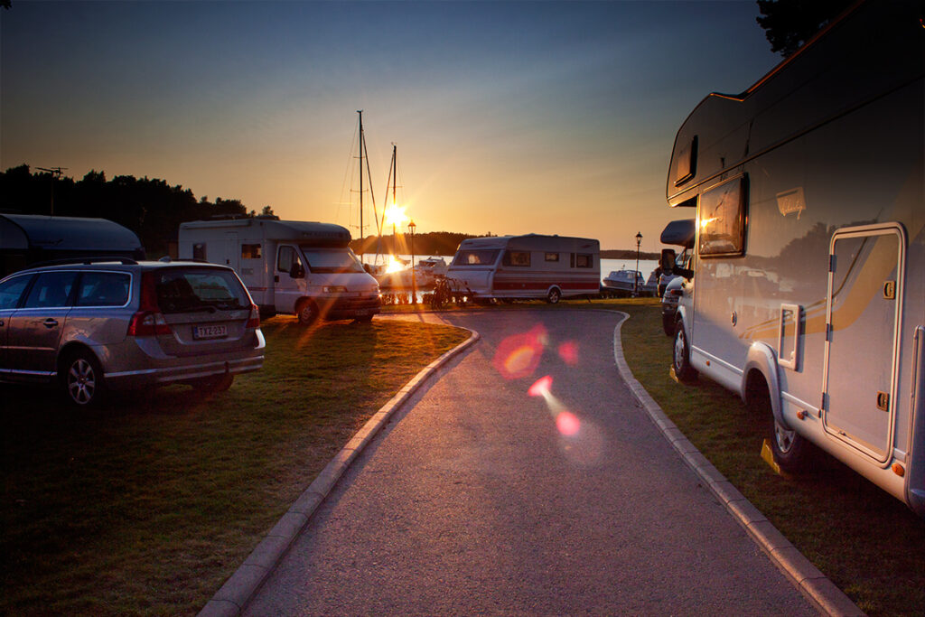 Matkailuautoja auringonlaskussa Poroholman leirintäalueella.