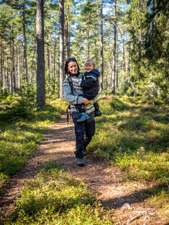 A person carrying a child on their hands in a forest path