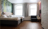 Sleep@Rauma hotellin hotellihuone, jossa kaksi ikkunaa, parisänky ja nojatuoli.